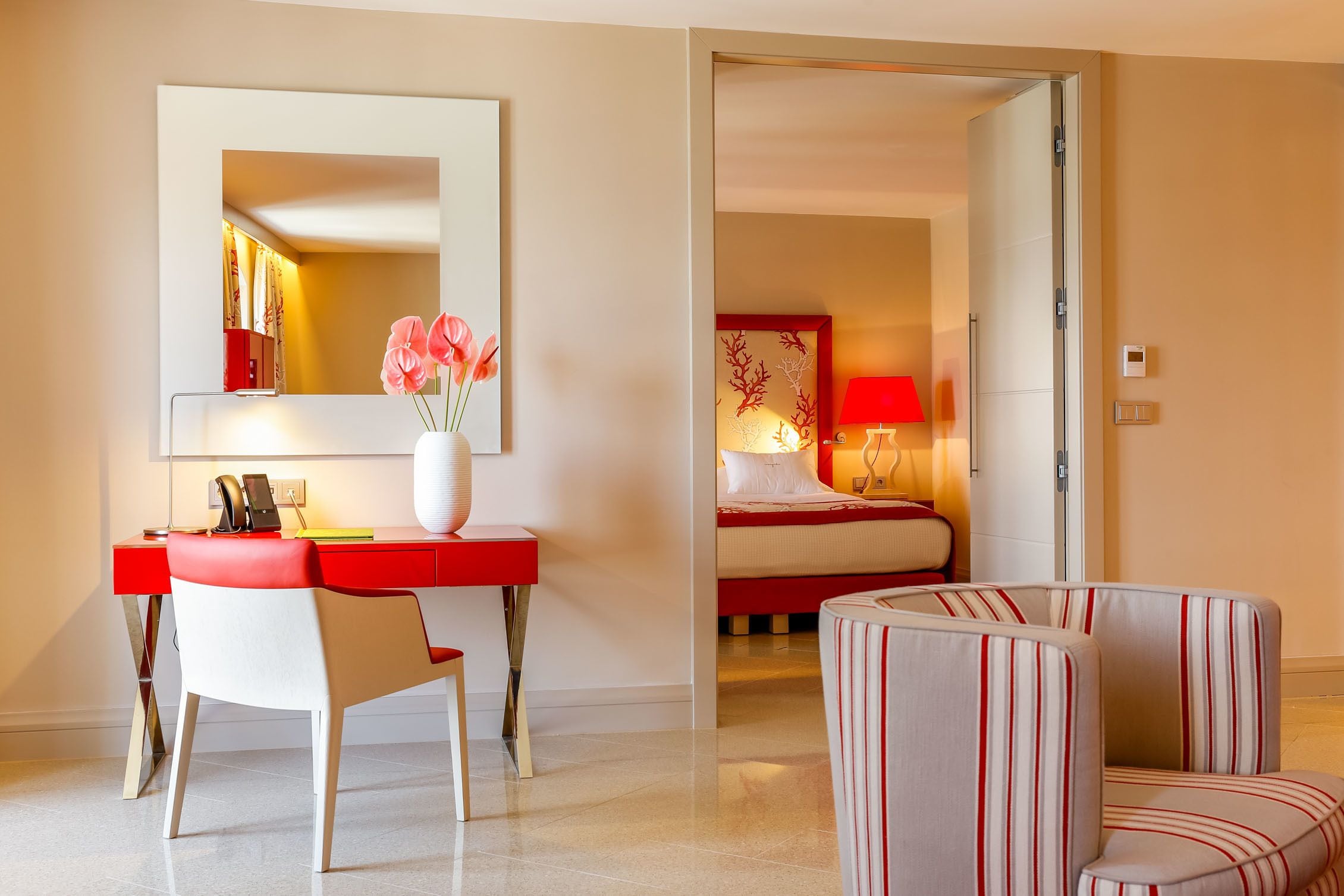 A hotel room with a desk, chair, and a bed with a red lamp.