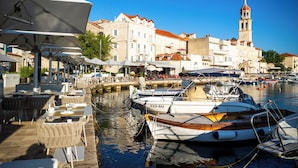 Un port de plaisance avec des bateaux amarrés, un restaurant au bord de l’eau doté d’une terrasse, et un bâtiment historique surmonté d’un clocher, le tout formant un ensemble pittoresque.