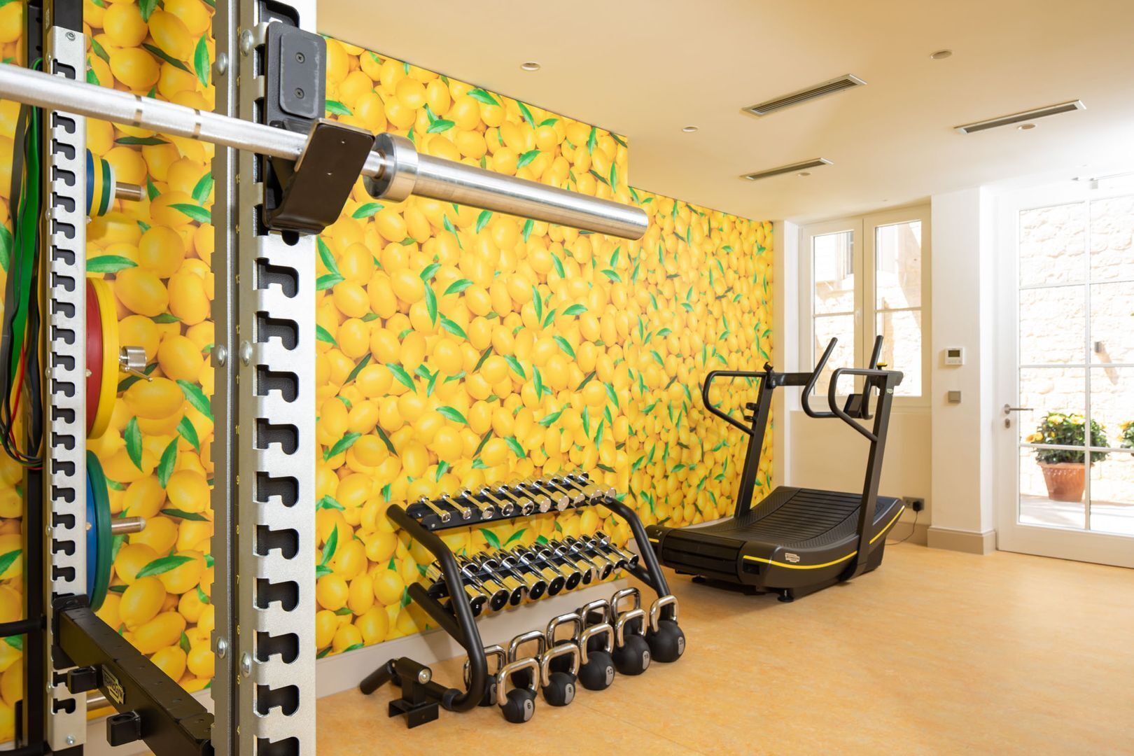 Un gimnasio con una cinta de correr, mancuernas y una pared decorada con limones.