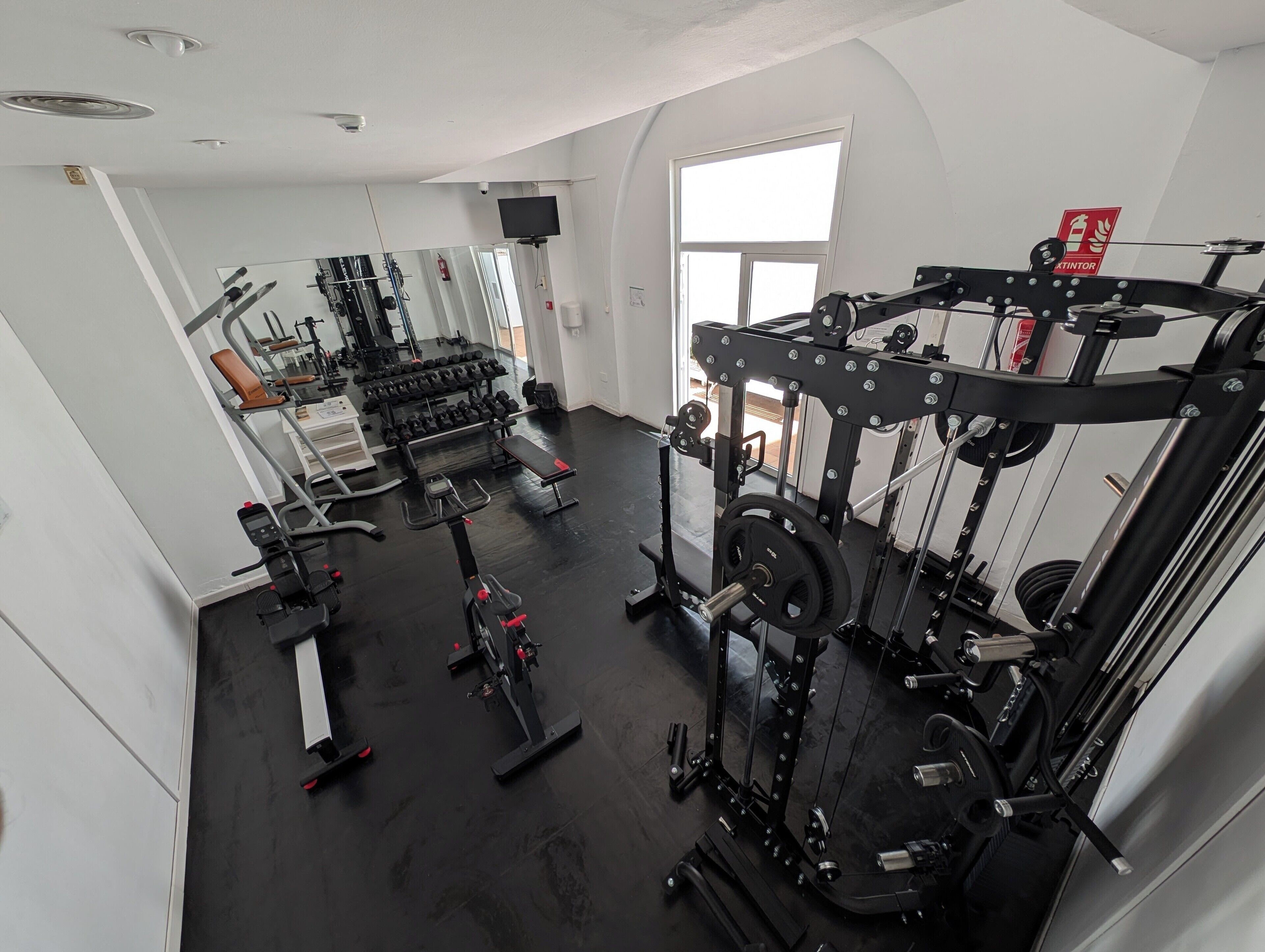 A gym with various exercise equipment, a large mirror, and a window providing natural light.