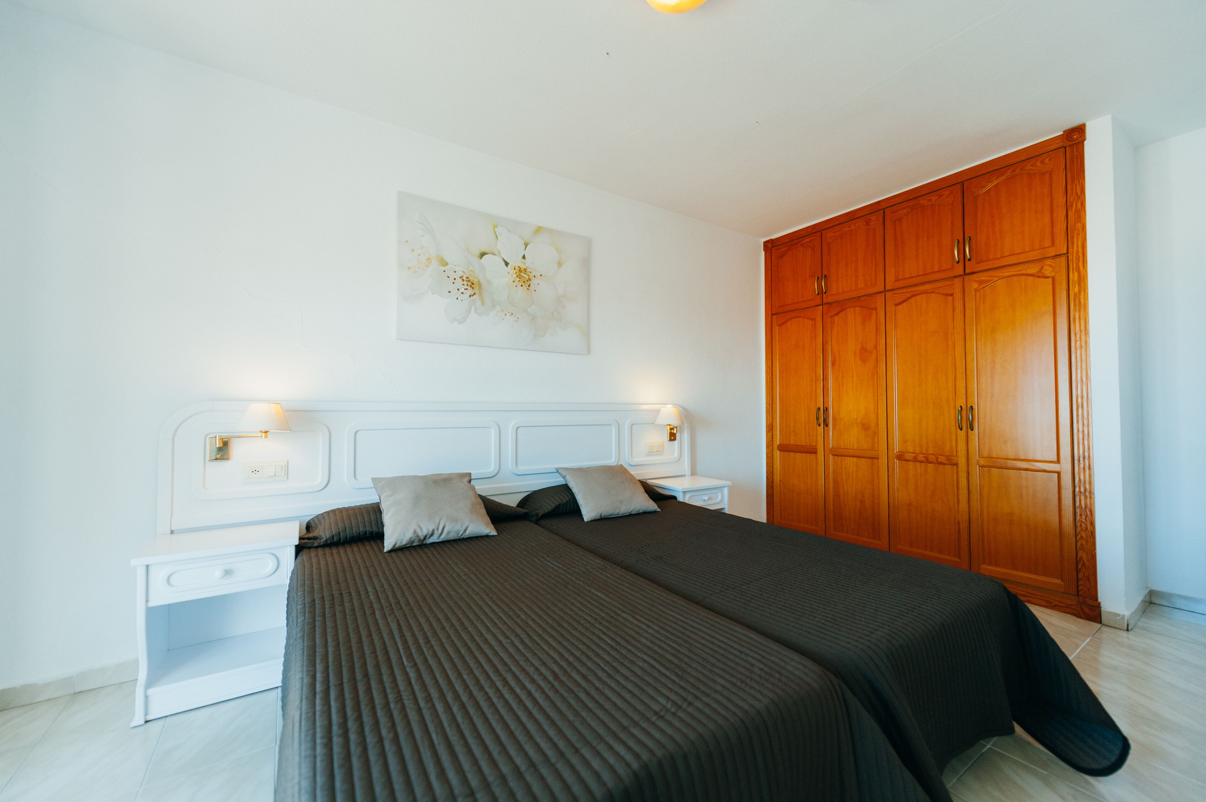 Ein Schlafzimmer mit einem großen Bett, einem Nachttisch, einem Holzschrank und einer Wandleuchte.