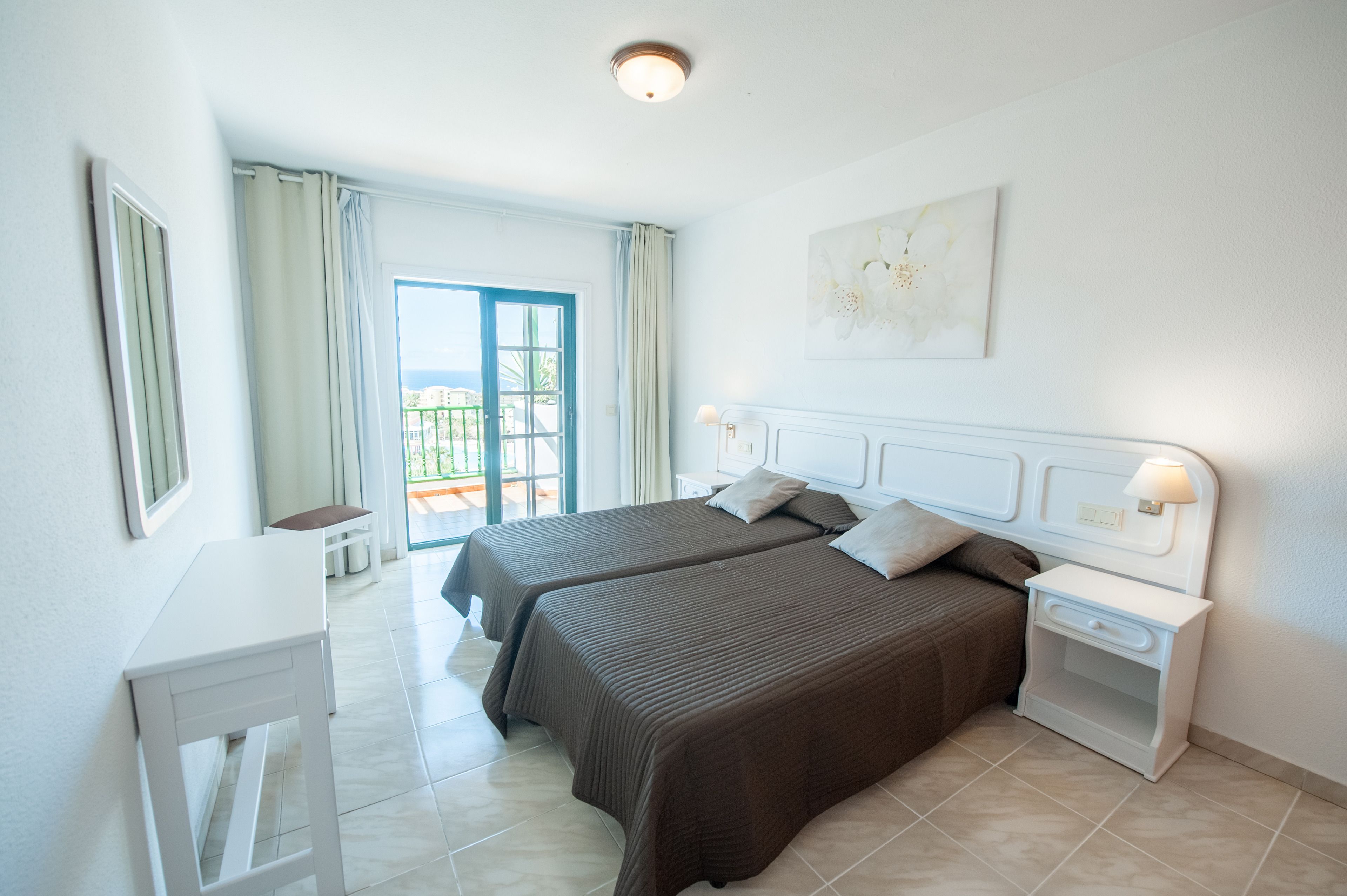 Habitación de hotel con dos camas, un escritorio, una mesita de noche y vistas al exterior.
