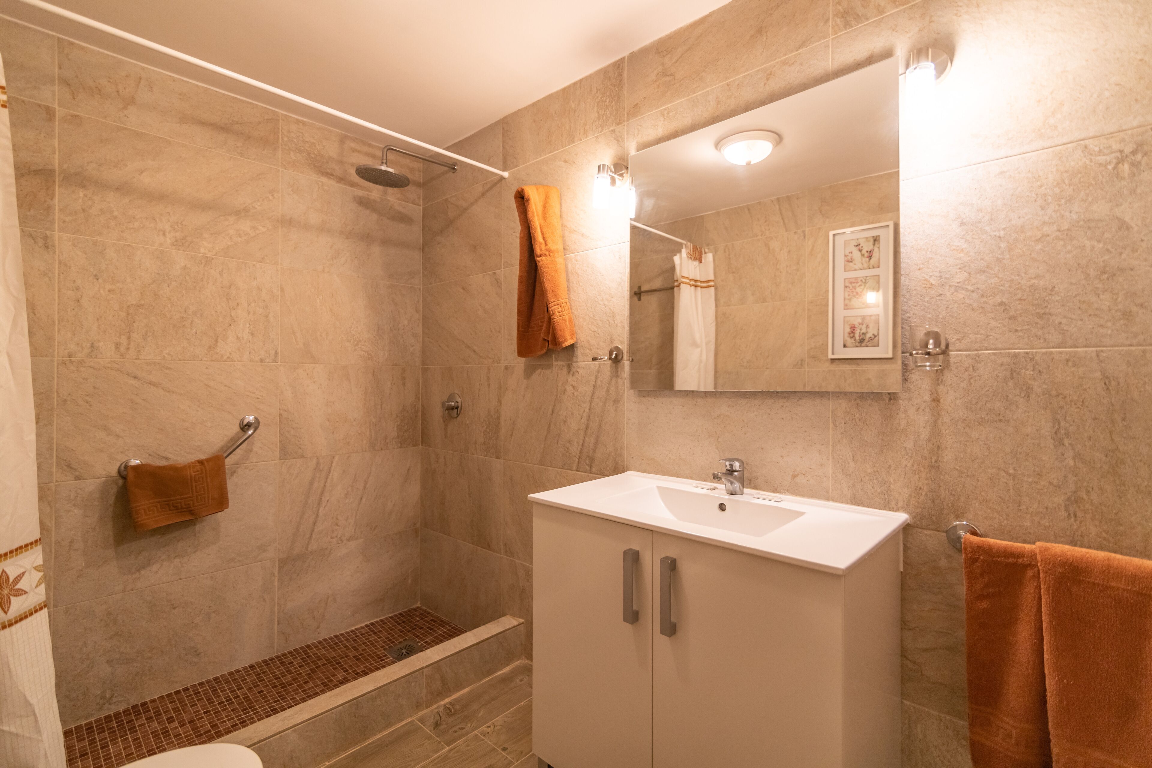 Un baño moderno con ducha, inodoro, lavabo y espejo.