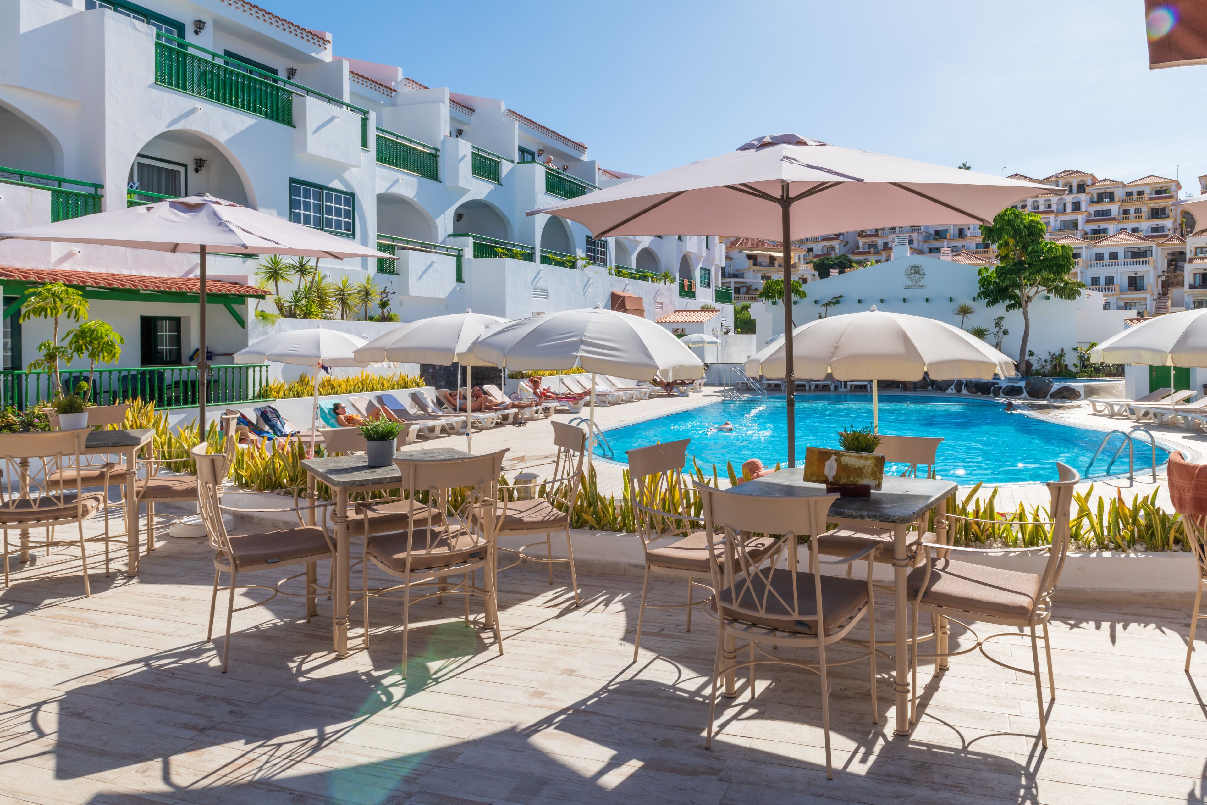 A poolside area with lounge chairs and umbrellas, surrounded by white buildings with green balconies.