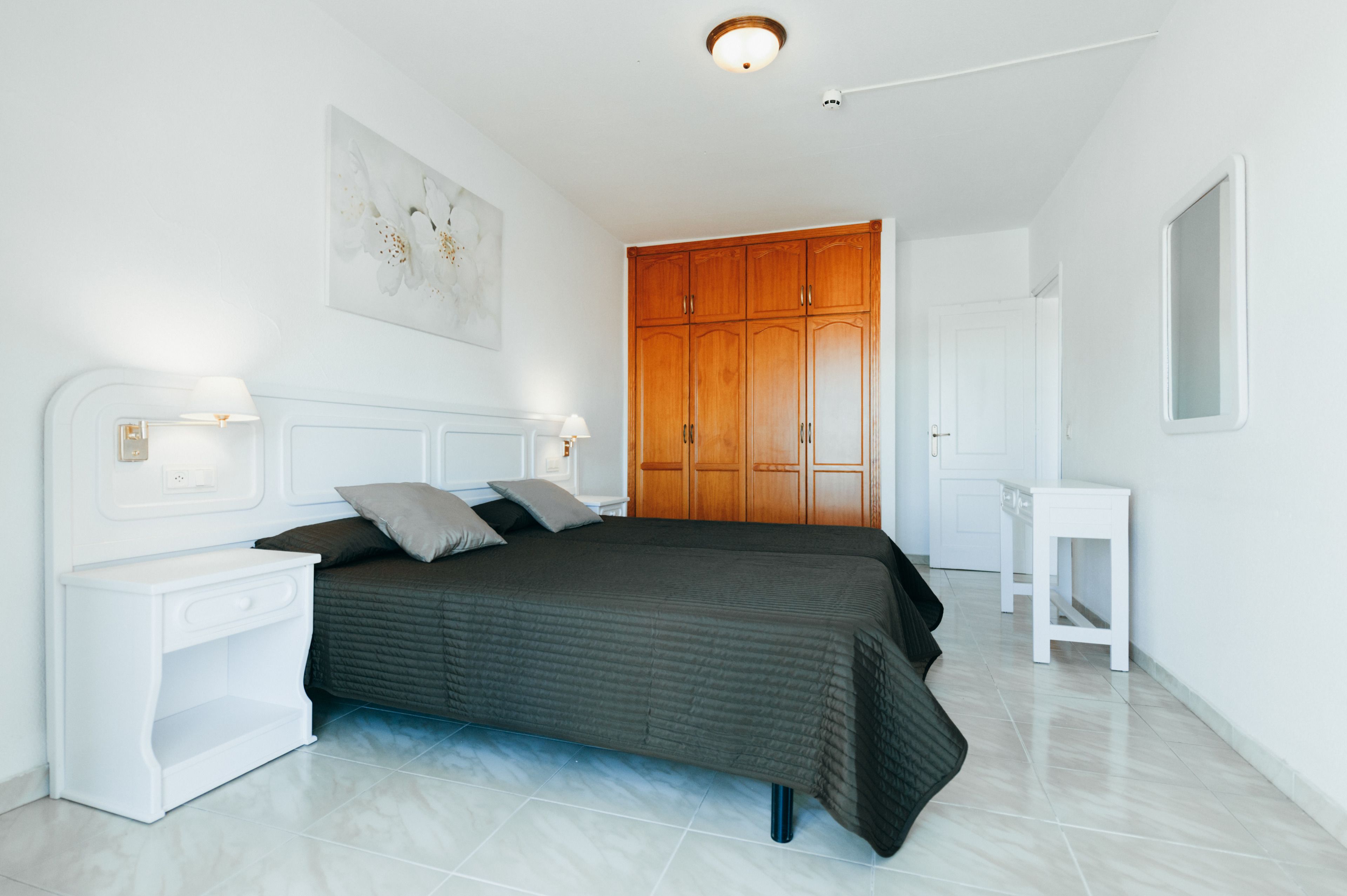 A bedroom with a bed, nightstands, a wooden wardrobe, and a small white table.