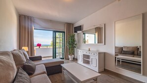 Ein modernes Wohnzimmer mit einer Couch, einem Couchtisch, einem Fernseher und einem großen Fenster mit Vorhängen.