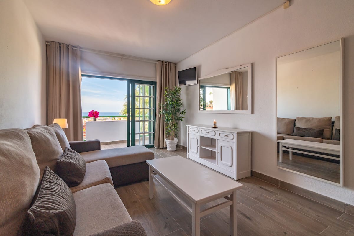Un salon moderne avec un canapé, une table basse, un téléviseur et une grande fenêtre avec des rideaux.