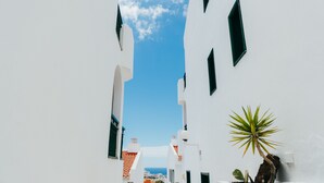Eine enge Straße mit weißen Gebäuden und grünen Fensterläden, die zu einem Blick auf das Meer führt.
