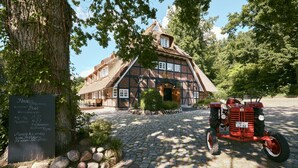 Un bâtiment traditionnel avec un toit de chaume, un chemin de pierre et un vieux tracteur garé devant.