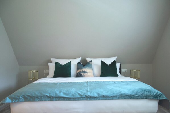 A neatly made bed with a blue and white duvet, two green pillows, and a single decorative pillow with a nature scene. - Meinsbur Boutique Hotel (Bendestorf)