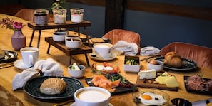 A wooden dining table with various breakfast items including bread, eggs, cheese, and smoked salmon. - Meinsbur Boutique Hotel (Bendestorf)