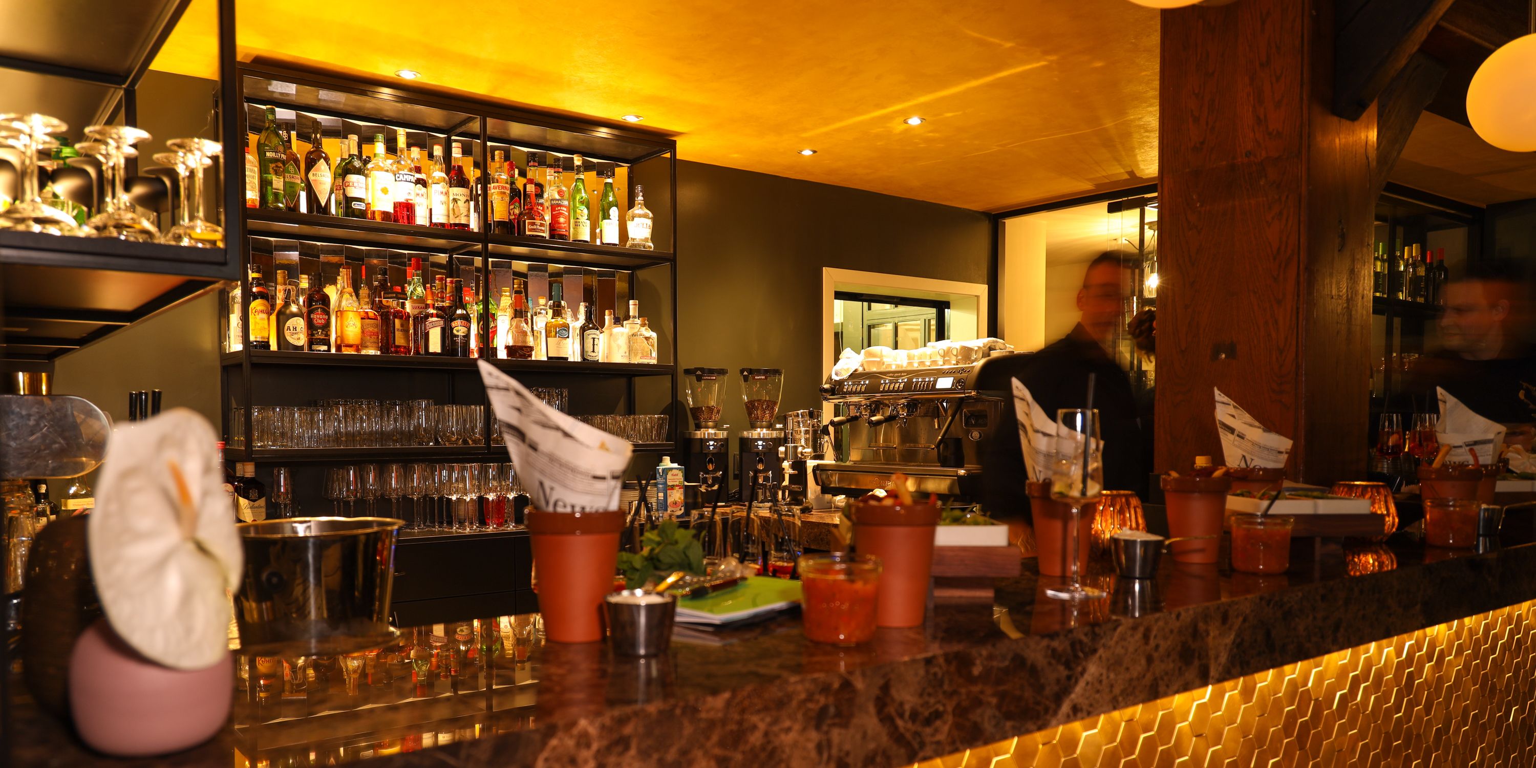 A bar area with shelves of liquor bottles, glasses, and a coffee machine.