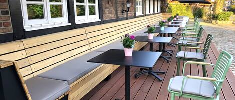 An outdoor seating area with wooden benches and tables, some with potted plants.