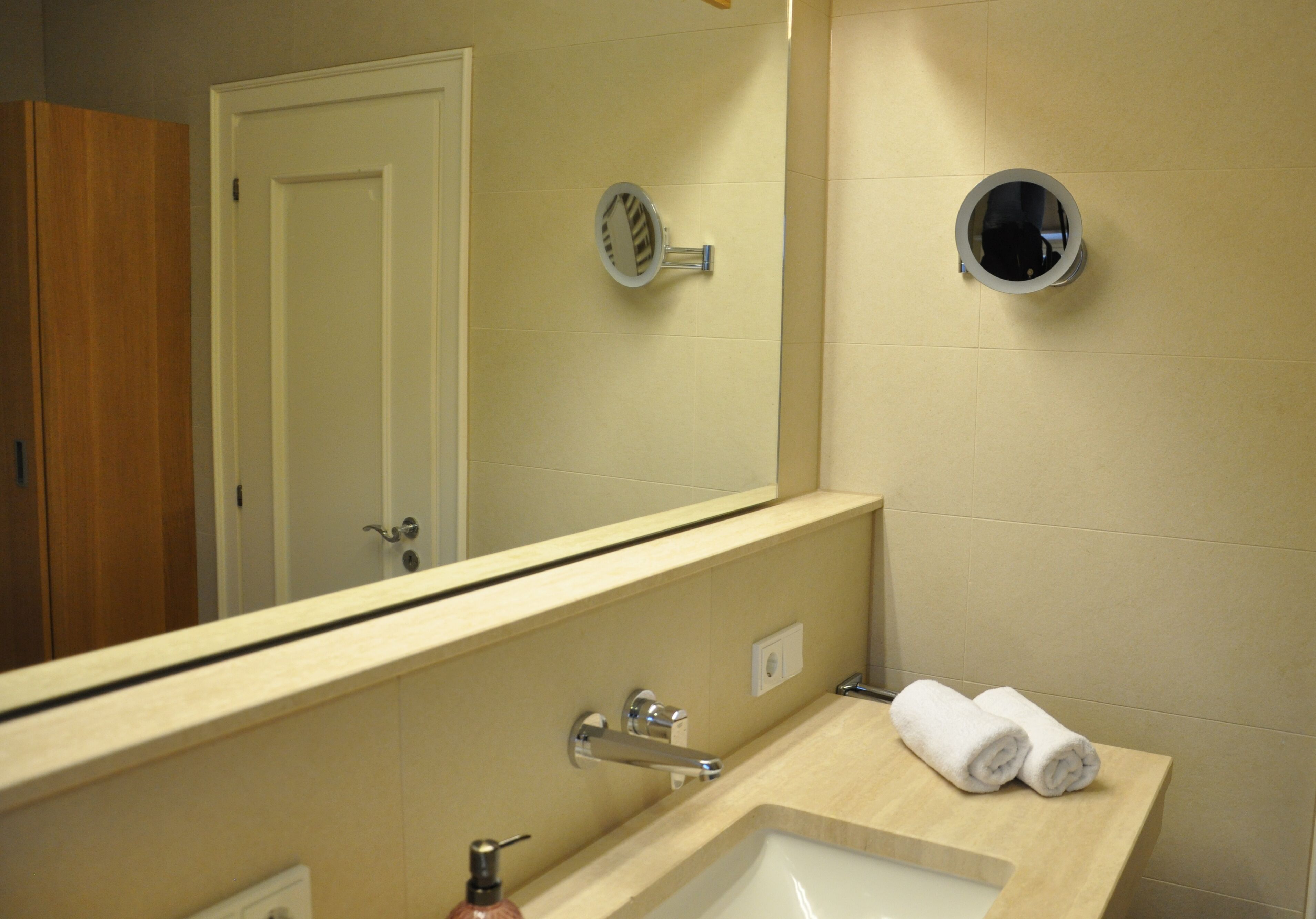 Une salle de bain équipée d’un lavabo, d’un miroir, d’un distributeur de serviettes et d’une porte.