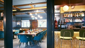 Un restaurant doté d’une longue table conviviale, de chaises bleues et d’un bar avec des tabourets.