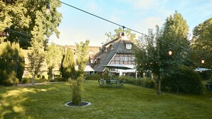 Une maison traditionnelle avec un toit en pente, entourée d’une pelouse bien entretenue et d’arbres.