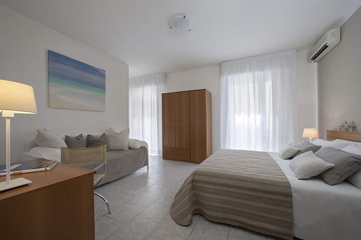 A modern hotel room with a bed, a sofa, a desk, and a wardrobe.