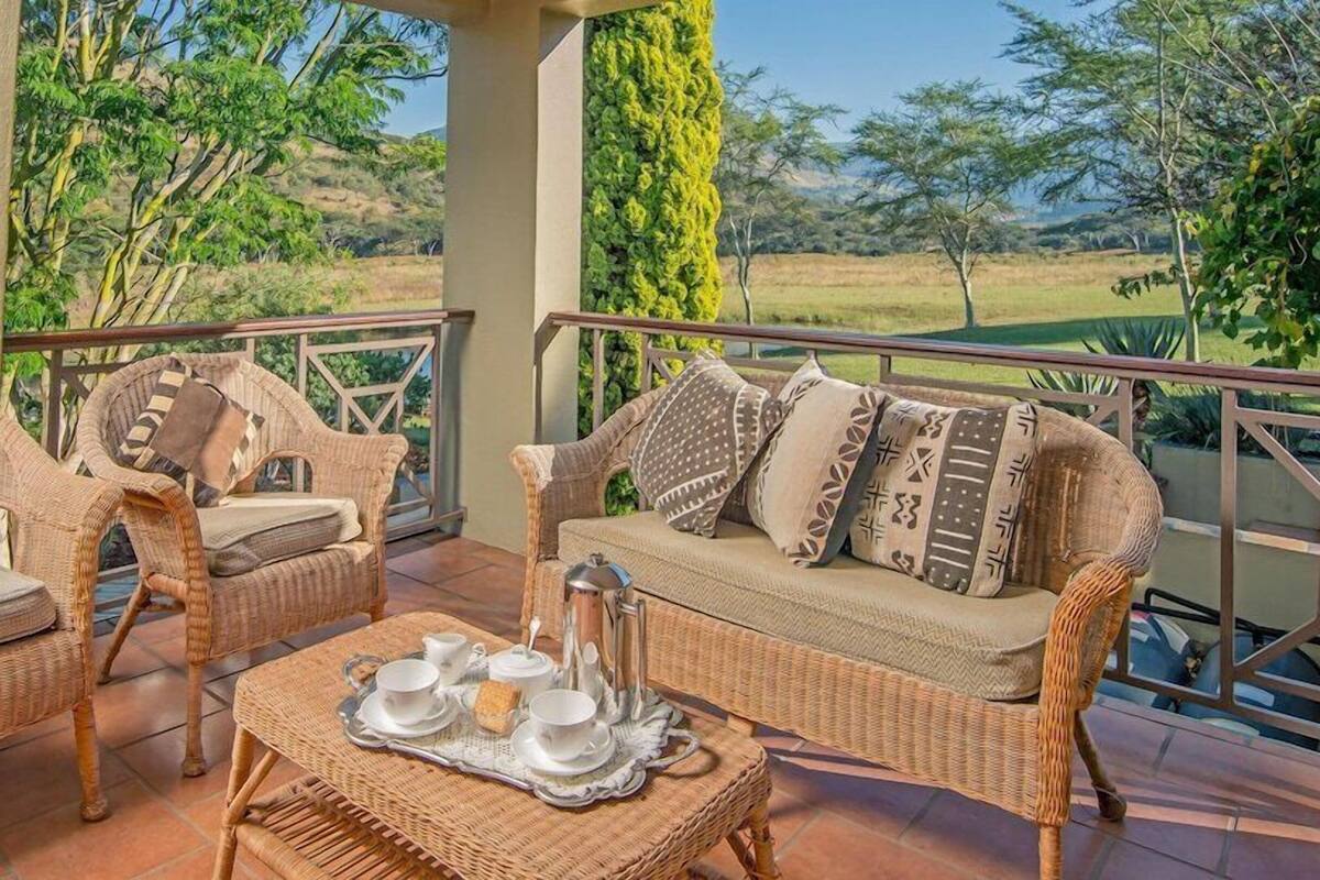 A balcony with wicker furniture, a tray with tea set, and a view of a grassy landscape.