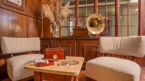 A room with two armchairs, a small wooden table, a red box, and a gramophone. - Saragossa Game Reserve (Emgwenya)