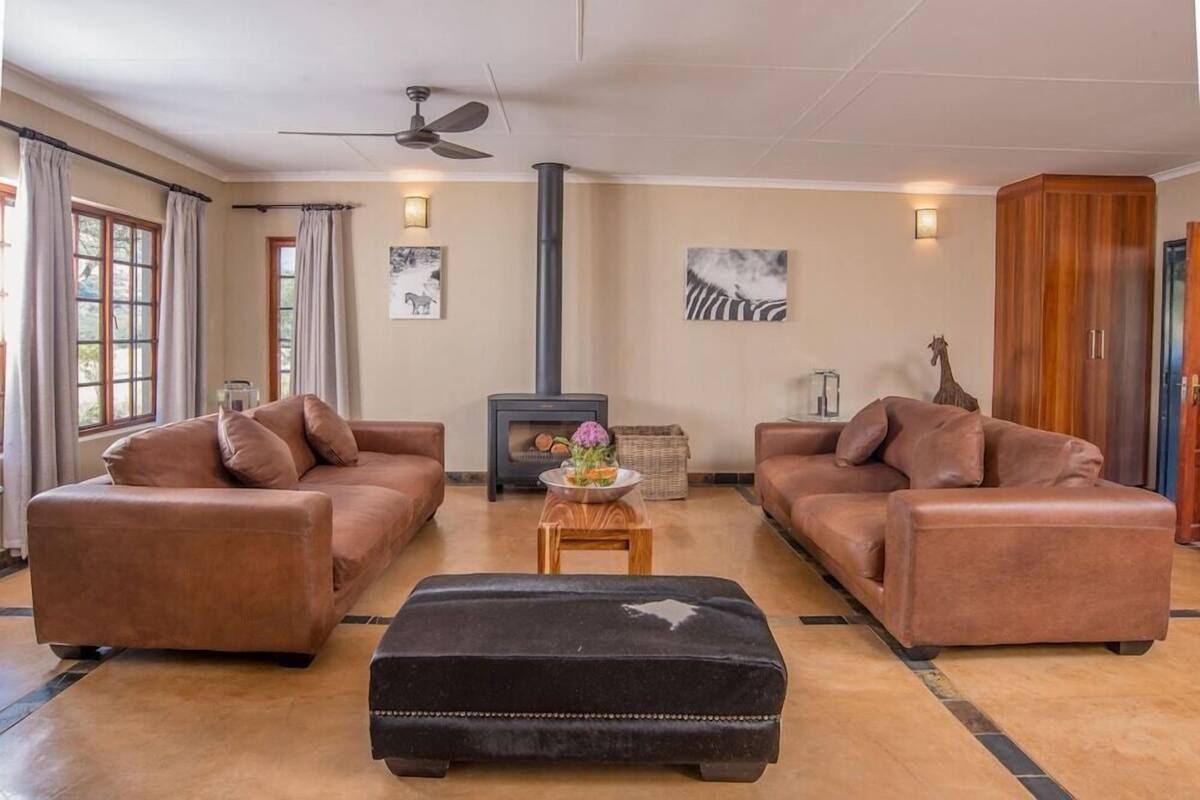 A living room with two brown leather sofas, a black ottoman, a fireplace, and a ceiling fan.