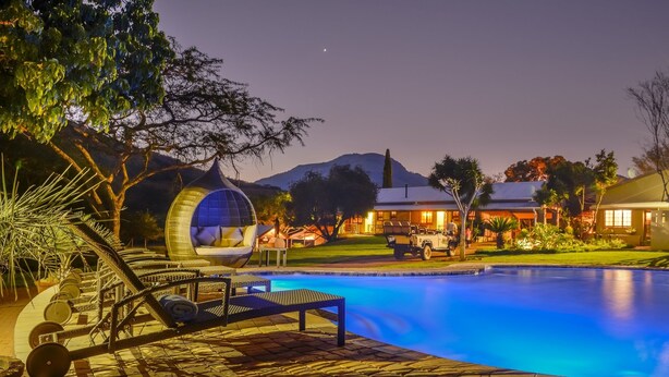 A pool area with a hanging chair, lounge chairs, and a building in the background. - Saragossa Game Reserve (Emgwenya)