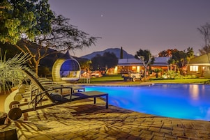Zona de piscina con una hamaca colgante, sillones de descanso y un edificio al fondo.