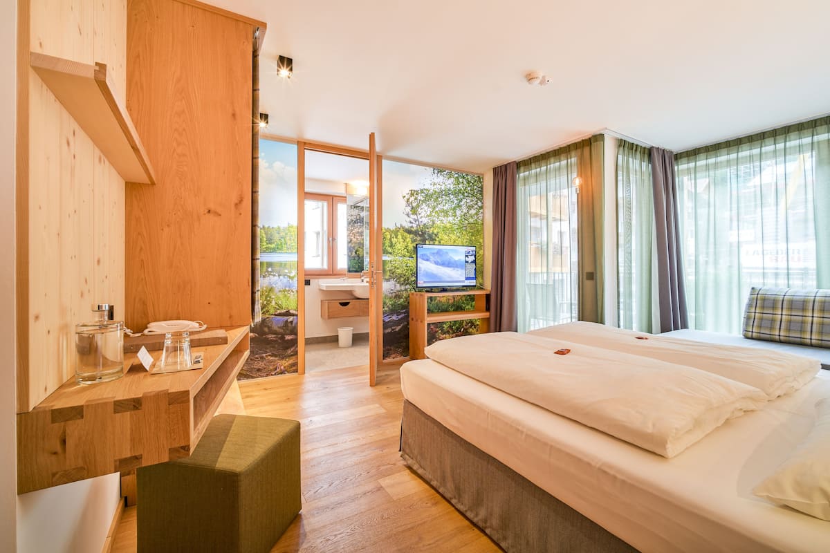 Une chambre d’hôtel moderne, dotée d’un bureau en bois, d’un lit, d’une télévision et offrant une vue sur l’extérieur.