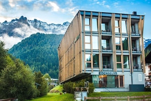 Un hotel moderno con fachada de madera, balcones y montañas al fondo.