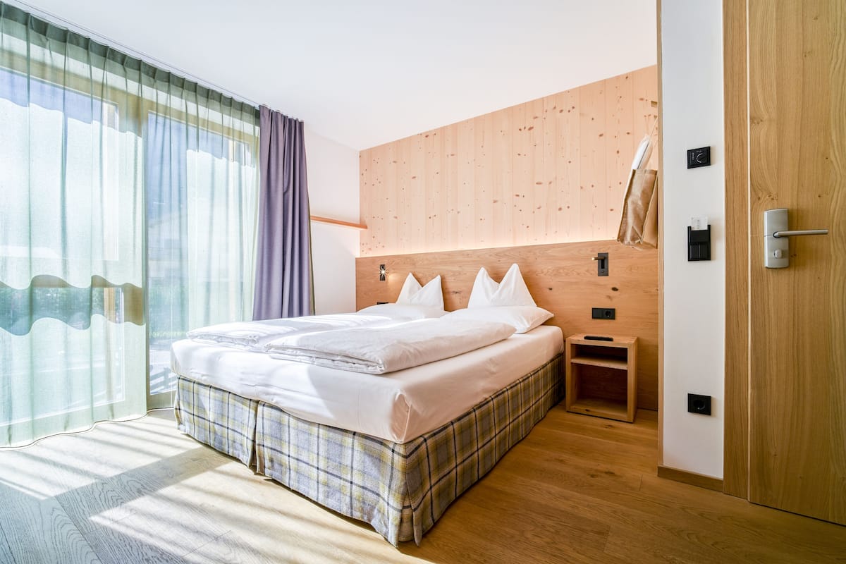 Une chambre d’hôtel moderne avec un grand lit, une tête de lit en bois et une armoire en bois.