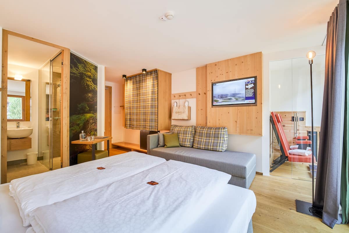 Une chambre d’hôtel moderne avec un grand lit, un canapé, une petite table et un téléviseur.