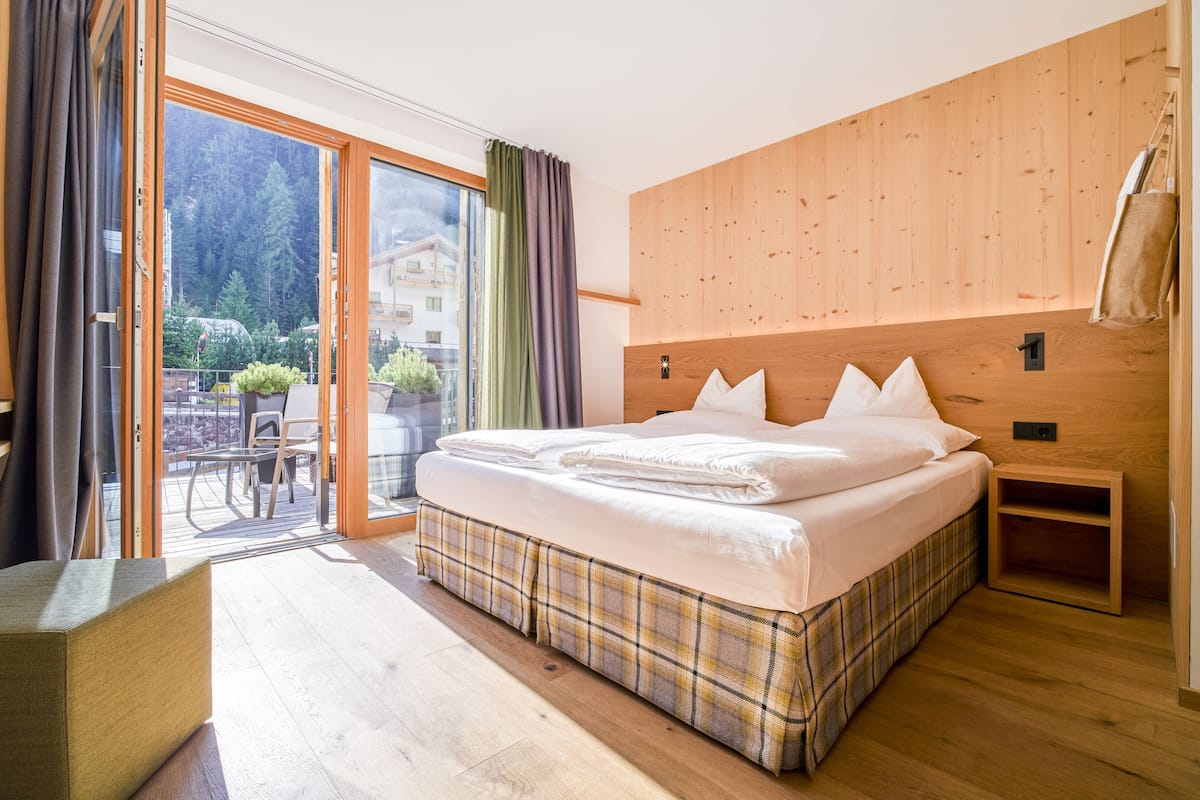 Une chambre à coucher avec une tête de lit en bois, un grand lit recouvert de linge de lit blanc, une table de chevet en bois et une porte-fenêtre coulissante donnant sur un espace extérieur avec une table et des chaises.
