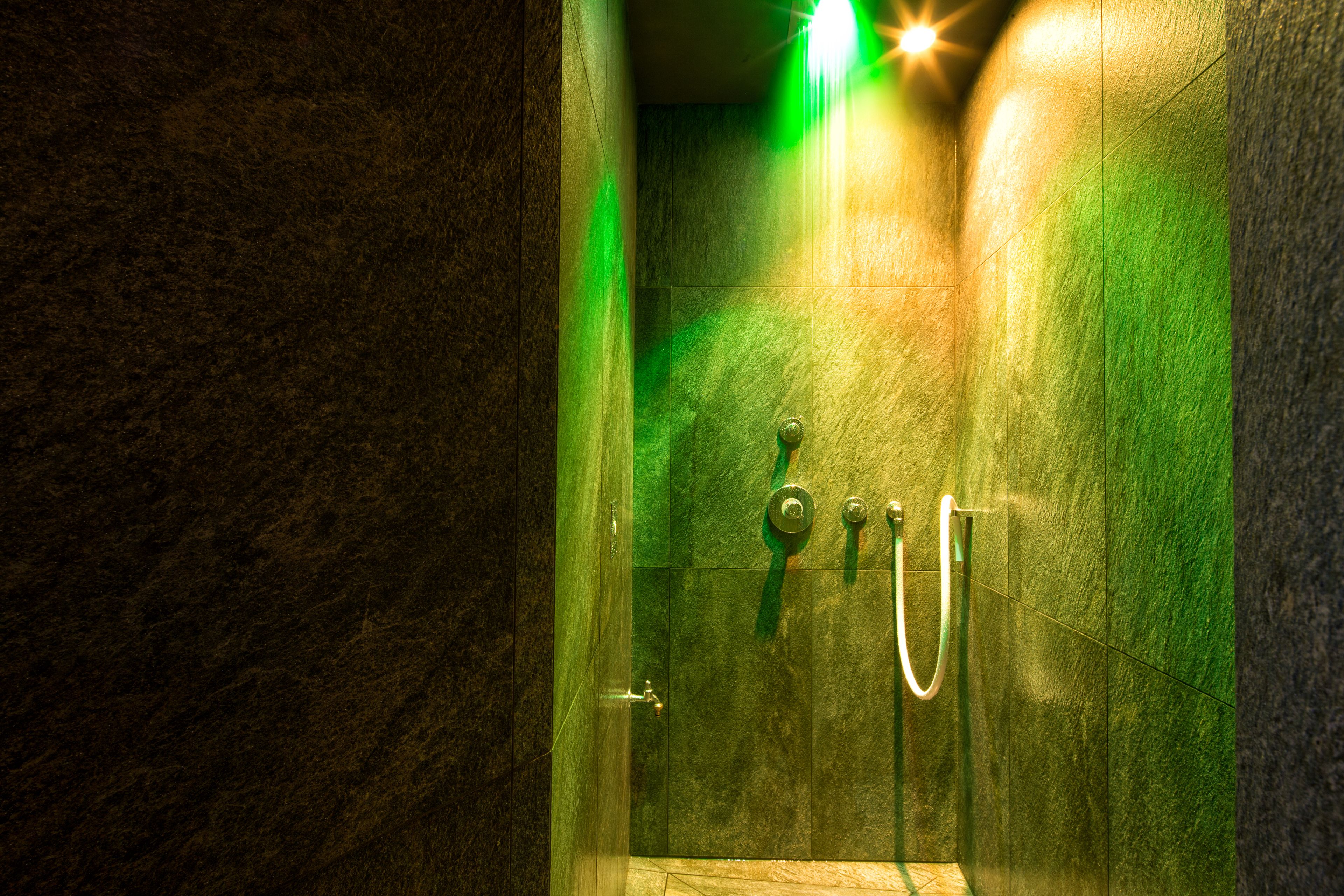Una ducha con paredes de vidrio, una luz verde, un cabezal de ducha y una perilla de control.