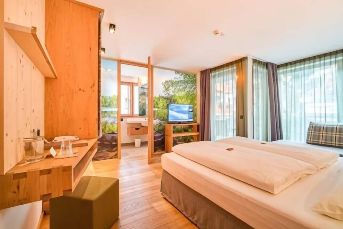 Une chambre d’hôtel moderne avec un bureau en bois, un lit, une télévision et une vue sur la verdure.