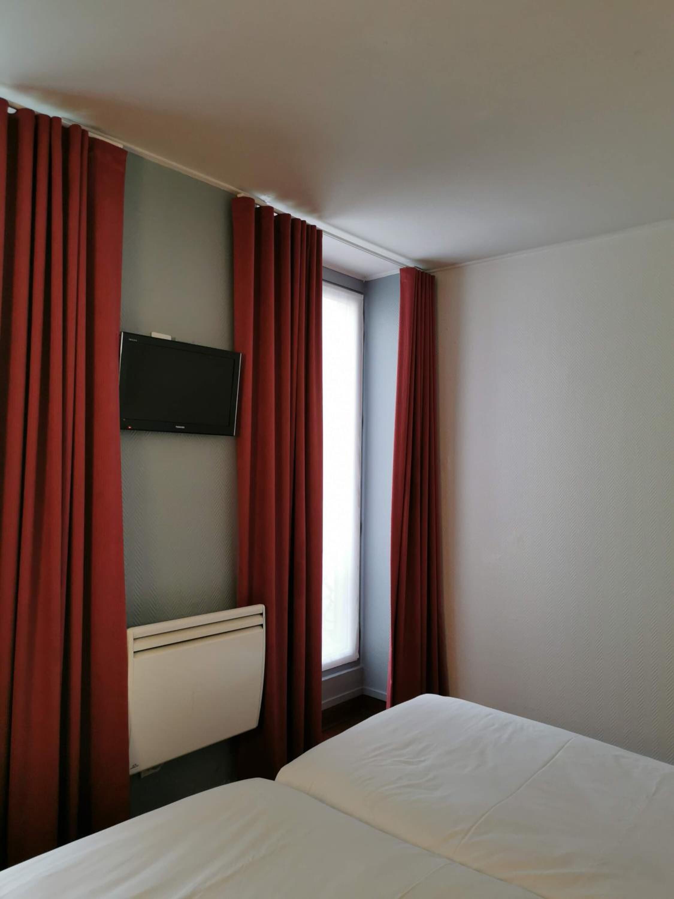 A hotel room with a bed, a TV mounted on the wall, and red curtains.