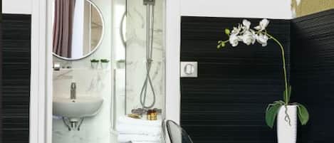 Une salle de bain moderne avec une douche à l’italienne en verre, un lavabo blanc et un meuble-lavabo en bois agrémenté d’un vase de fleurs blanches.
