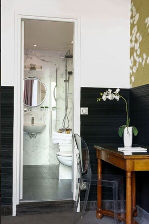 A modern bathroom with a glass shower enclosure, a white sink, and a wooden vanity with a vase of white flowers. - Hôtel Victoria Paris (Paris)