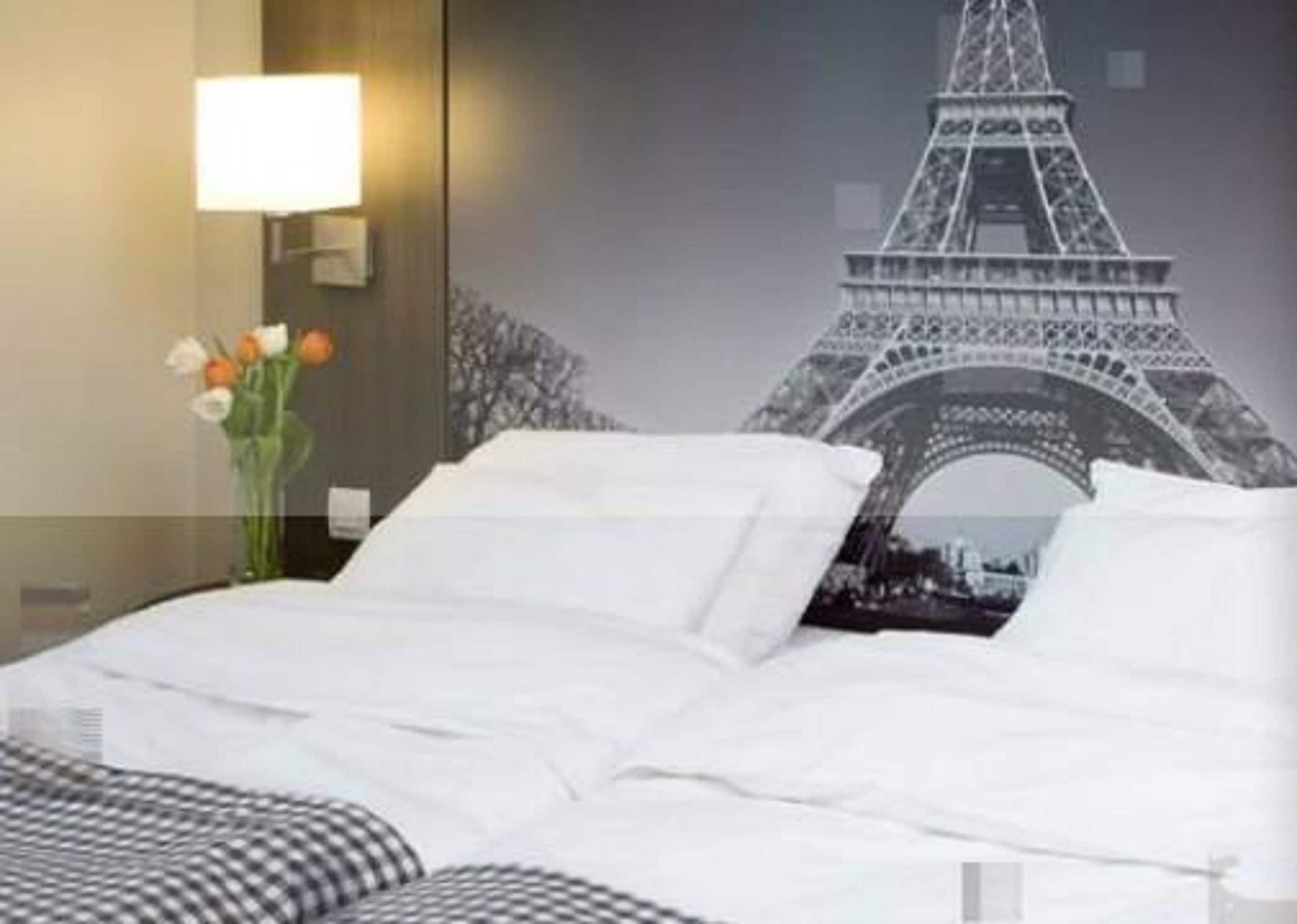 Une chambre d’hôtel avec un lit, une table de chevet avec une lampe et un mur orné d’une grande image de la Tour Eiffel.