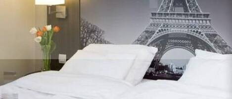A hotel room with a bed, a nightstand with a lamp, and a wall with a large Eiffel Tower image.