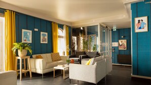 A modern living room with a sofa, armchairs, and a coffee table. There are potted plants and artwork on the walls. - Hôtel Victoria Paris (Paris)