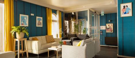 A modern living room with a sofa, armchairs, and a coffee table. There are potted plants and artwork on the walls.