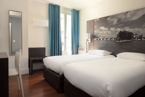 A hotel room with two beds, a desk, and a large window with curtains. - Hôtel Victoria Paris (Paris)