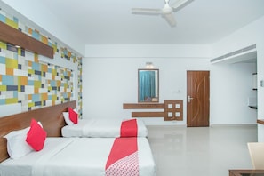 A hotel room with two beds, a ceiling fan, a mirror, and a wooden door. - Collection O 3175 Pluspoint Suites (Bengaluru)