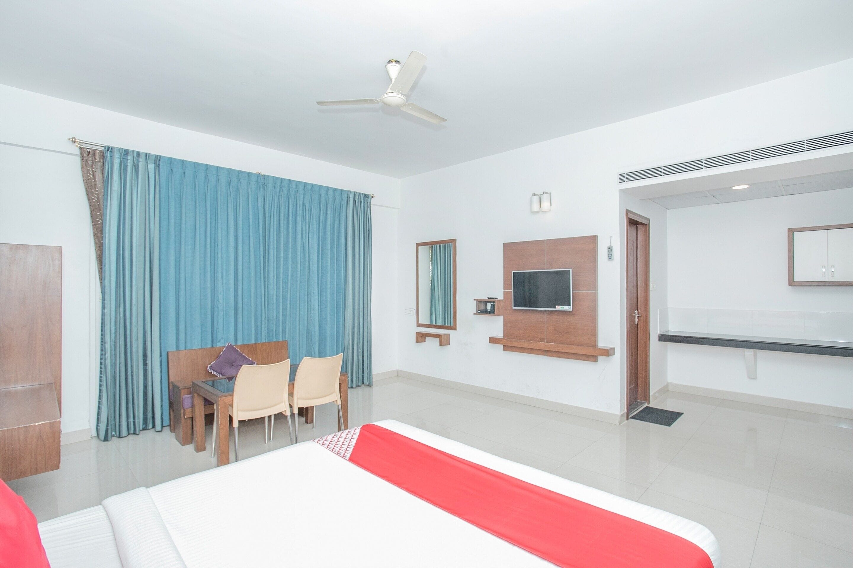 Ein Hotelzimmer mit einem Bett, einem Schreibtisch mit Stühlen, einem Fernseher und einem Deckenventilator.