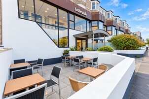 An outdoor seating area with tables and chairs, a building with a sign reading 'Lothersdale,' and a clear sky.