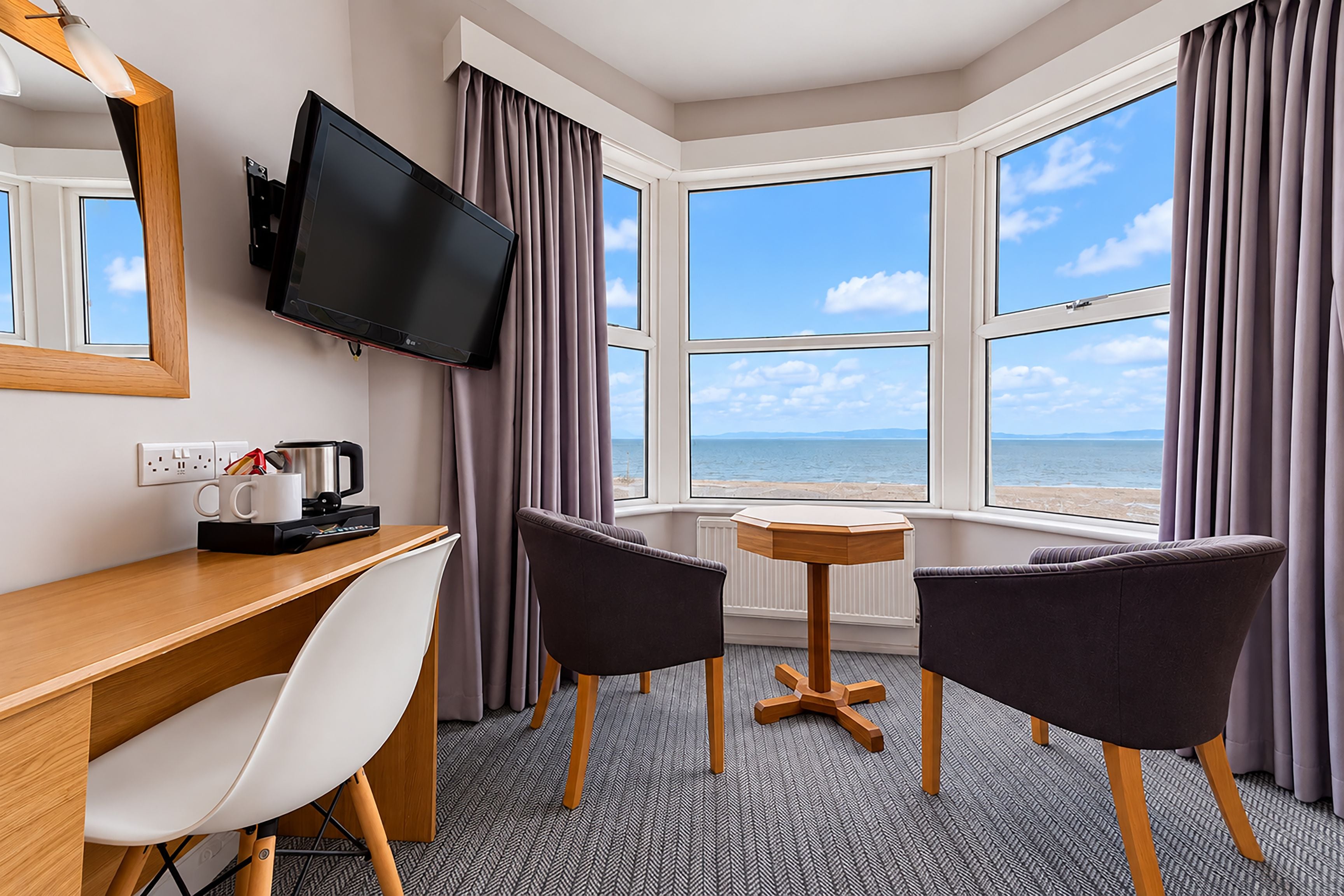 A hotel room with a desk, two chairs, a television, and a view of the sea.