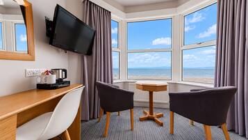 Habitación de hotel con escritorio, dos sillas, televisor y vista al mar.