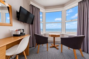 A hotel room with a desk, two chairs, a television, and a view of the sea.