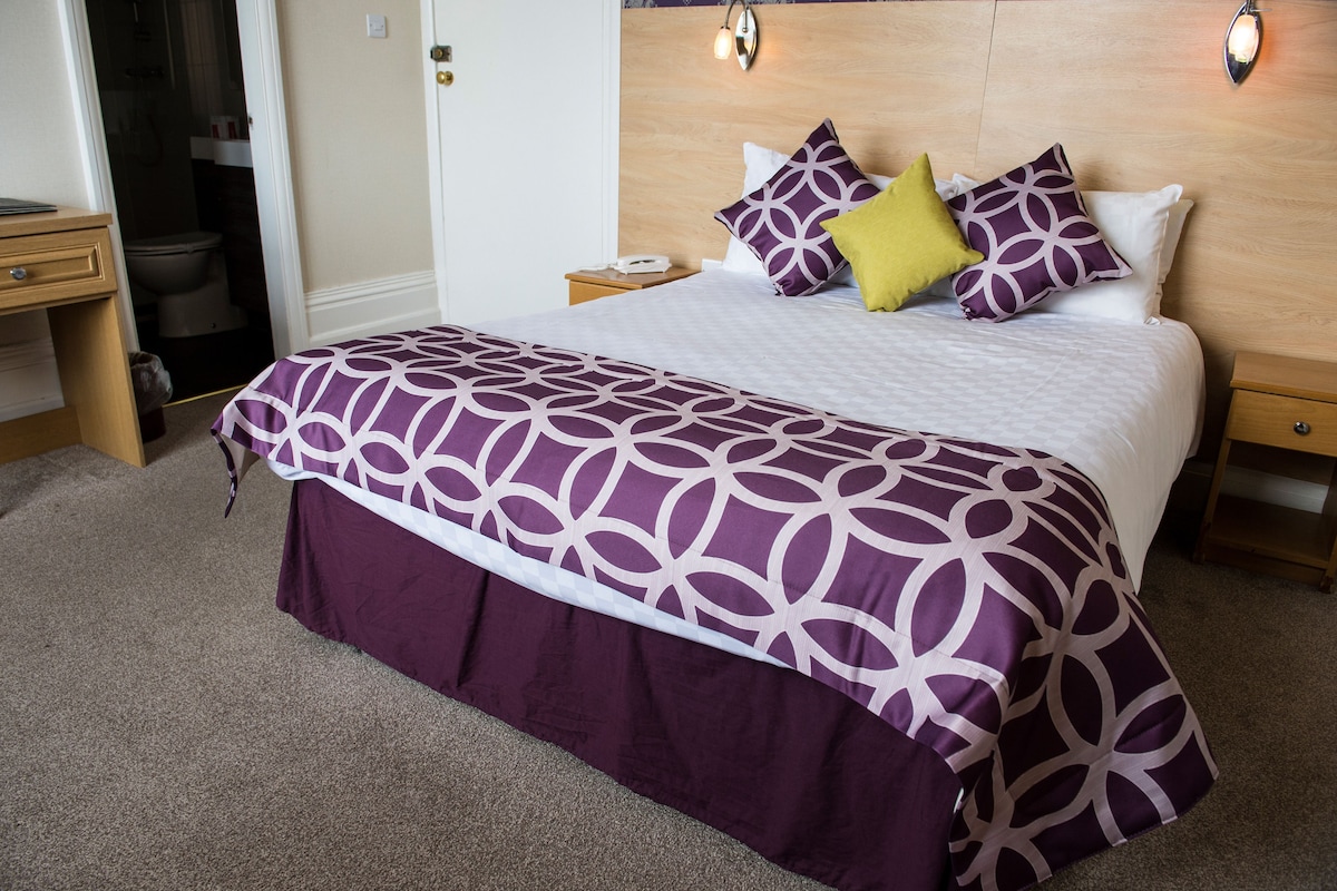 A neatly made bed with a patterned bedspread, a bedside table with a lamp, and a wooden headboard.