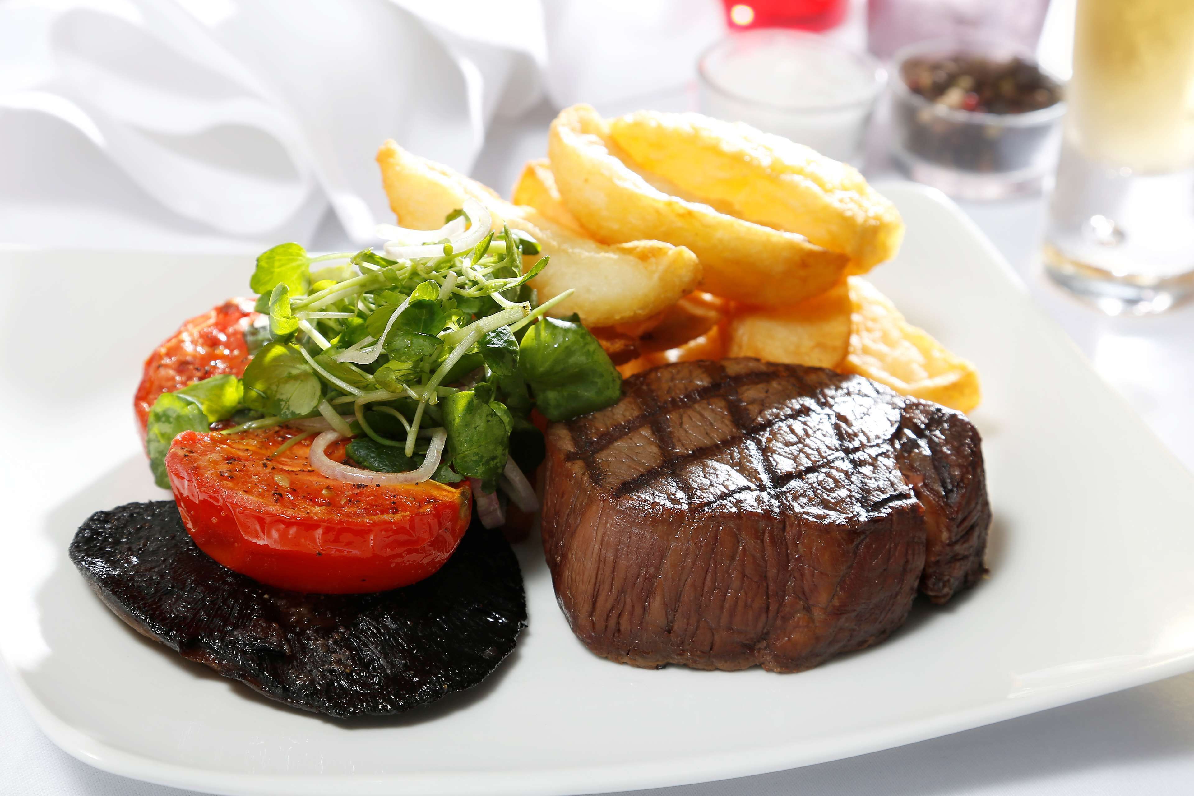 Une assiette avec un steak, des frites, une tomate et des légumes verts.