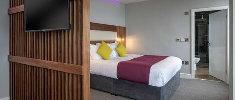 Een moderne hotelkamer met een groot bed, een flatscreen televisie bevestigd aan een houten paneel en een badkamer die door een geopende deur zichtbaar is.